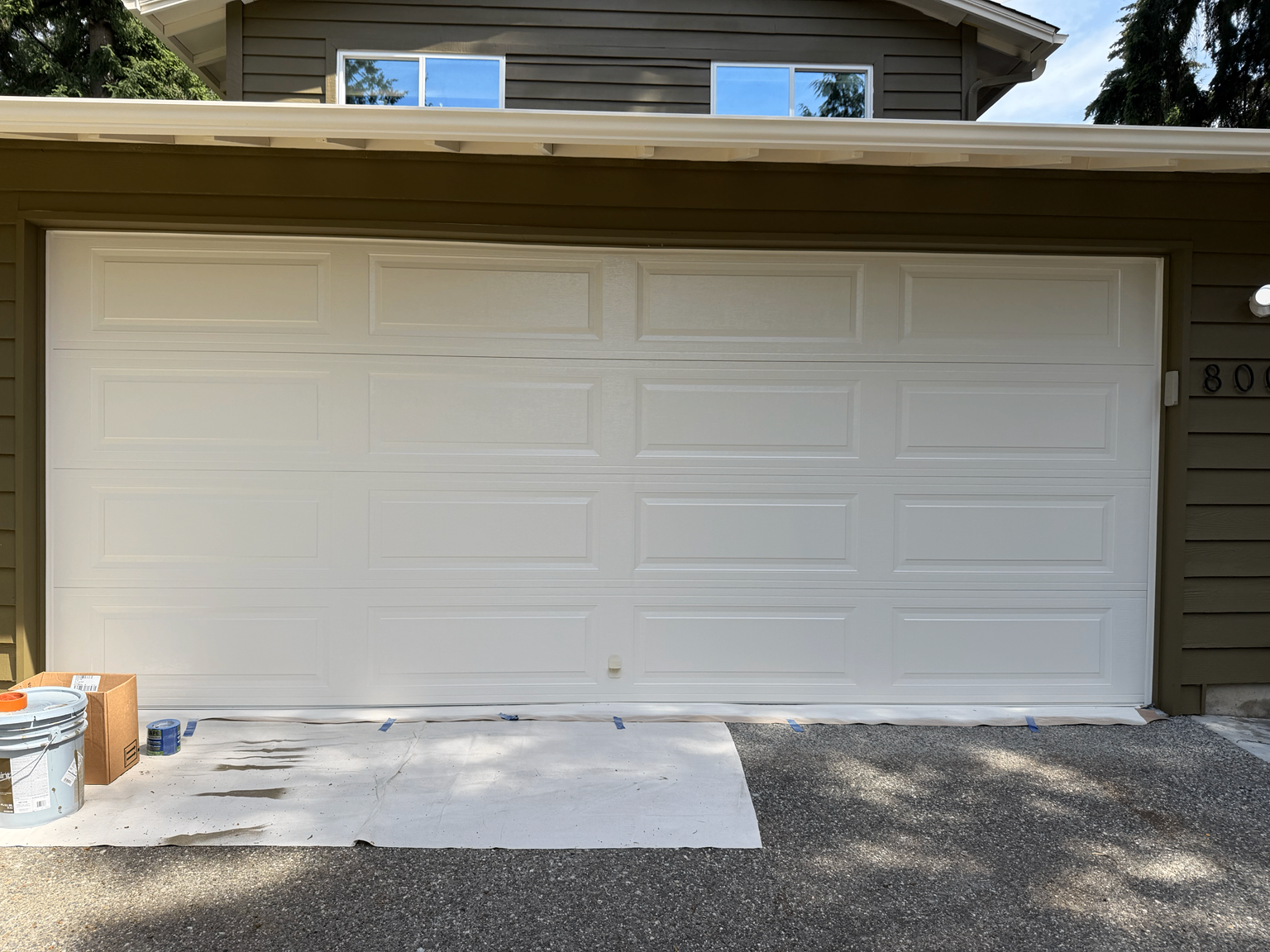 Close-up of a freshly finished white garage door on an olive-green home exterior