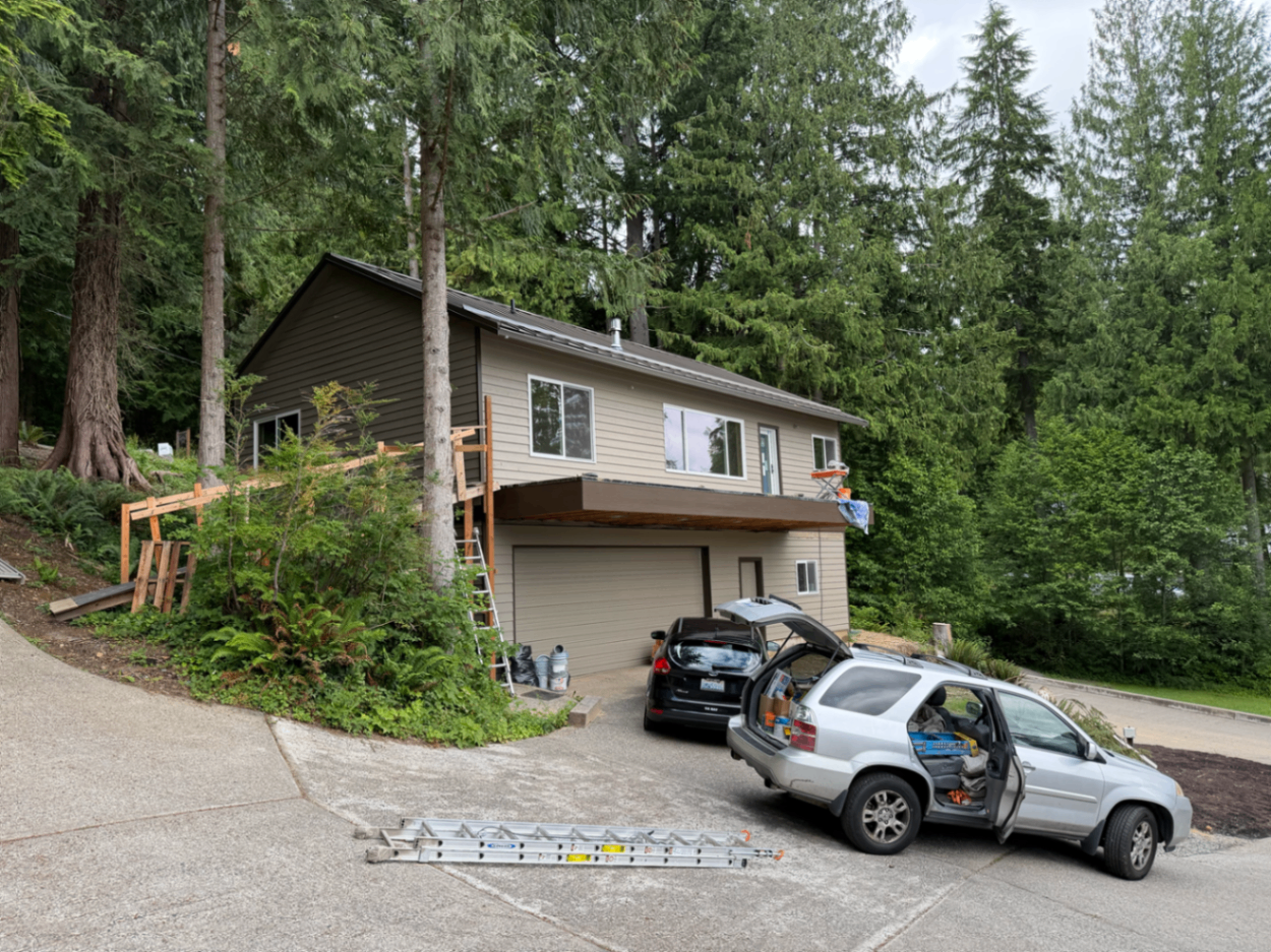 Completed front angle of a custom lakefront home with fresh exterior paint and wooded backdrop