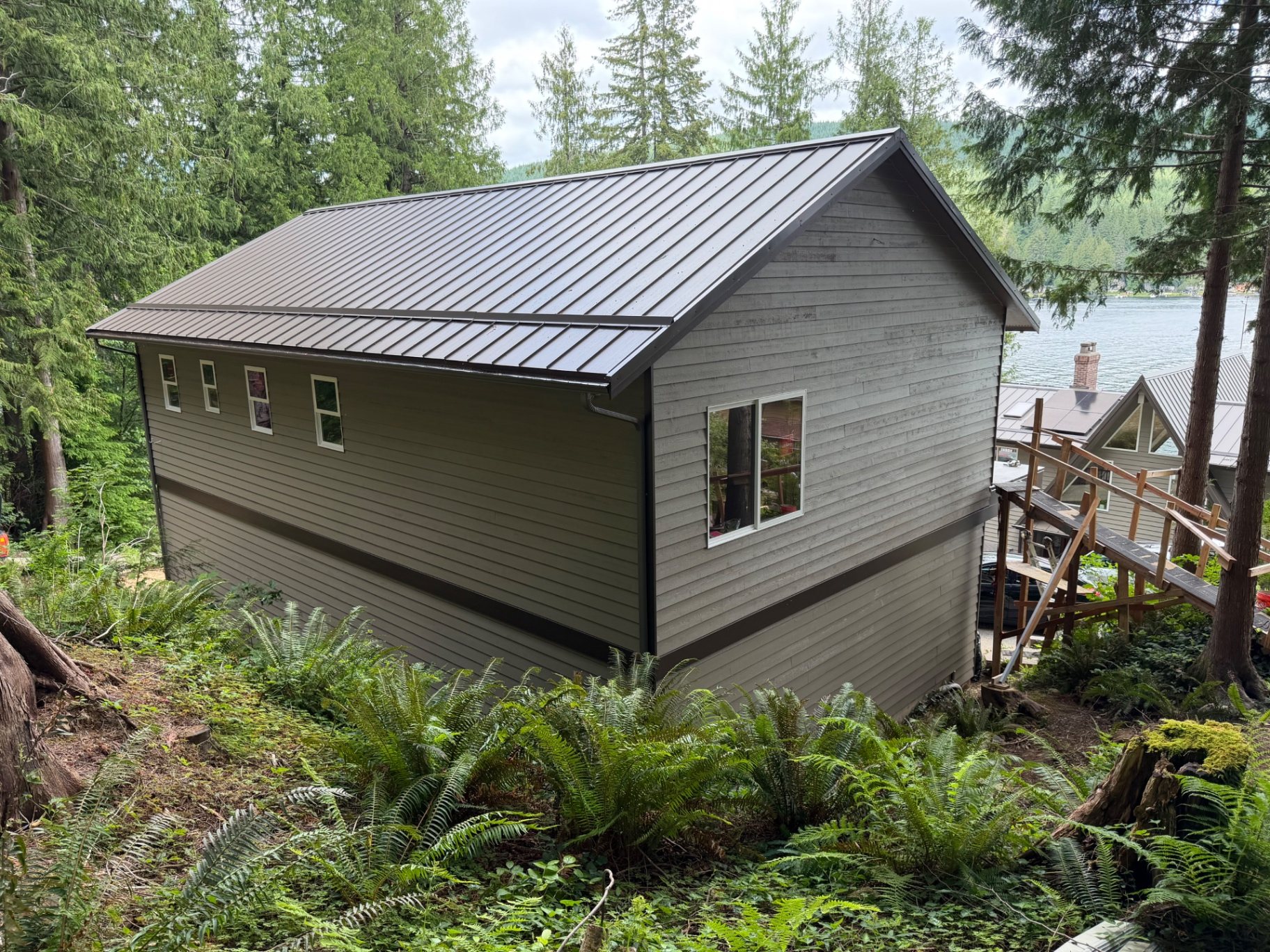Completed lakefront custom home viewed from the rear, with a dark metal roof overlooking the lake