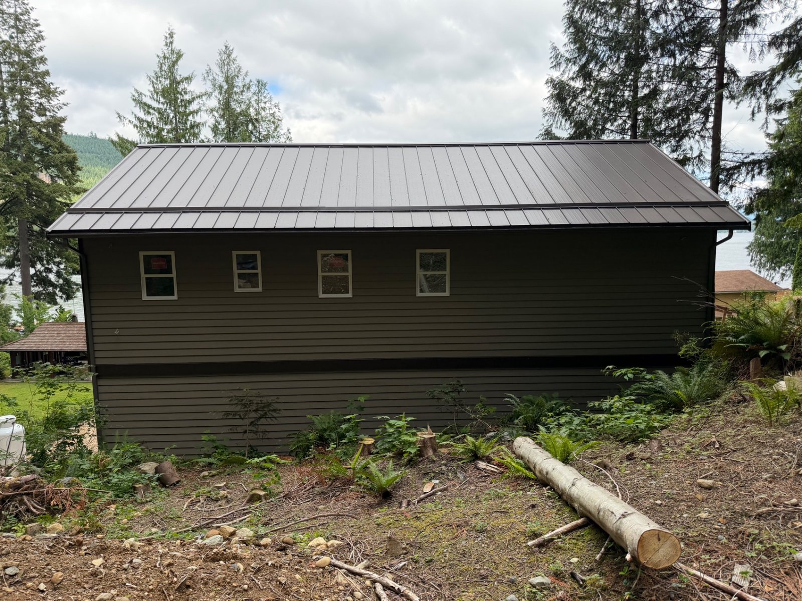 Completed side elevation of a lakefront custom home with dark olive siding and metal roof beside the water